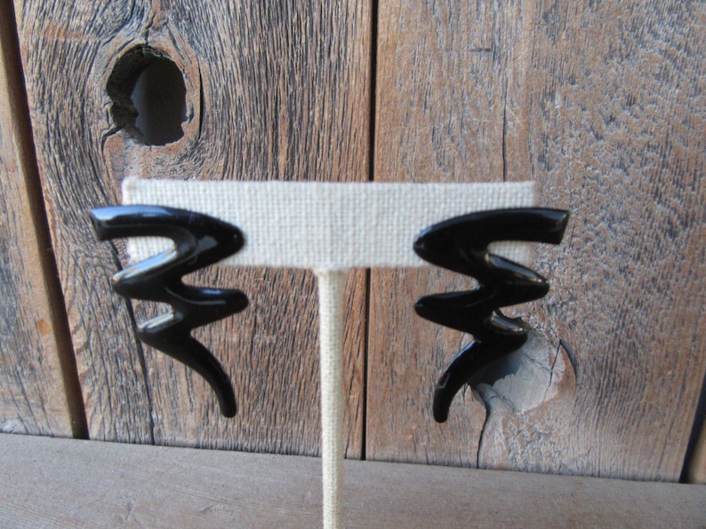 Pode incluir: Um par de brincos pretos de forma abstrata. Os brincos s&atilde;o feitos de um material liso e brilhante e t&ecirc;m um design geom&eacute;trico.