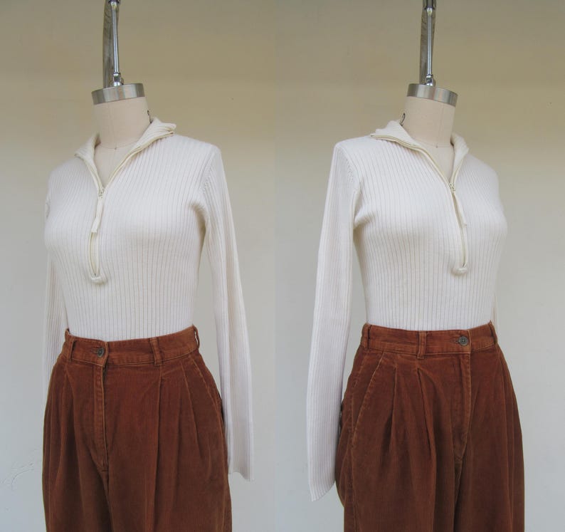 May include: A white ribbed sweater with a zipper neckline and long sleeves, paired with brown corduroy pants.