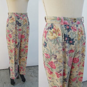 May include: Beige high-waisted pants with a floral print featuring pink, yellow, and blue flowers. The pants have a pleated front and a wide waistband.