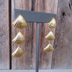 May include: Gold tone dangle earrings with three layered seashell charms.