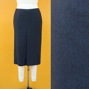 May include: A dark navy blue pencil skirt displayed on a mannequin. The skirt is knee-length with a slit in the back. The fabric appears to be a solid, textured material. The background is a bright yellow.