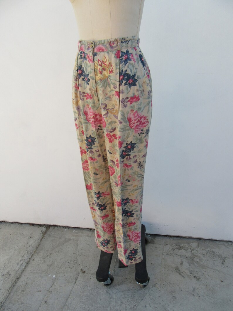 May include: High-waisted pants with a floral print featuring pink, yellow, blue, and green flowers on a beige background.