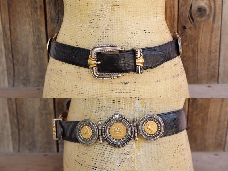 May include: Two black leather belts with decorative silver and gold buckles. The top belt has a large rectangular buckle with gold accents. The bottom belt features three circular medallions with gold-toned details and a central medallion with a horse design.