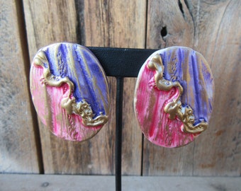 May include: A pair of oval-shaped earrings with a pink, purple and gold abstract design.