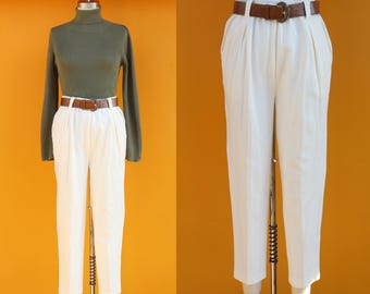 May include: White high-waisted pants with pleats and a brown belt. The pants are on a mannequin.
