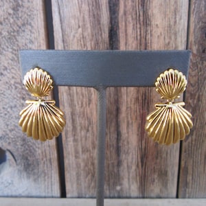 May include: A pair of gold-tone shell-shaped dangle earrings. The earrings are on a gray display stand.