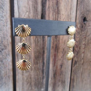 May include: Gold tone dangle earrings with three scallop shell charms on each earring.