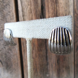 Puede incluir: Un par de pendientes de plata en forma de concha en un expositor blanco.