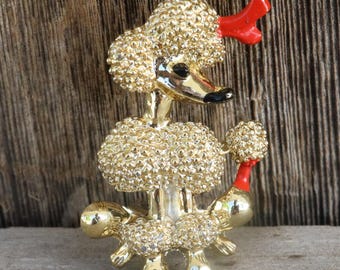 May include: Gold-tone brooch of a poodle with red bows. The poodle is covered in tiny gold beads.