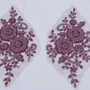 May include: Two matching decorative appliques. Each applique features a floral design with beaded and sequined accents in shades of pink and mauve. The appliques are set on a white mesh backing.