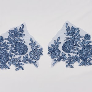May include: Two symmetrical blue floral lace appliques featuring intricate embroidery and small sequins on a sheer mesh backing. The floral motifs include swirling stems, leaves, and blossoms, creating a detailed decorative pattern for garment embellishment.