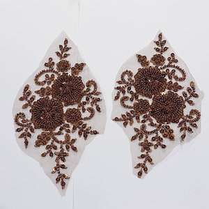 May include: Two brown sequined floral appliques on a white mesh background. The appliques feature a cluster of three flowers with intricate leaf details.