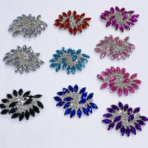 May include: Assortment of ten rhinestone embellishments in various colors, including silver, red, pink, blue, black, and purple. Each embellishment is shaped like a flower with a spiral design.