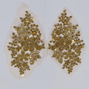 May include: Two gold floral appliques with sequins and beads on a white background.