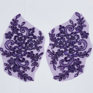 May include: Two purple lace appliques with a floral design. The appliques are made of a sheer fabric with a delicate floral pattern and are embellished with sequins.