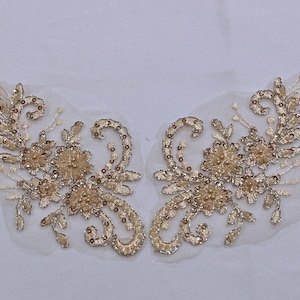 May include: Two gold floral appliques with pearl accents on a sheer white fabric background.