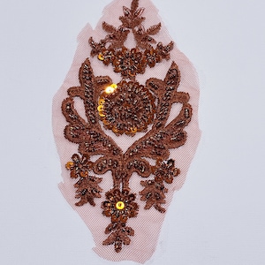 May include: A brown and gold sequined applique with a floral design. The applique is on a sheer fabric background.