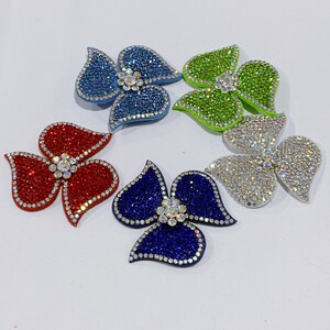May include: Six rhinestone flower embellishments in red, blue, green, and silver. Each flower has three petals and a central rhinestone cluster. The petals are covered in small, sparkling rhinestones.