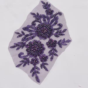 May include: Purple beaded floral applique with a mesh backing. The applique features a cluster of flowers with beaded centers and leaves.
