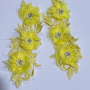 May include: Two yellow floral appliques. Each applique features three chiffon-like flowers with pearl and rhinestone centers, and embroidered leaves. The appliques are ideal for embellishing garments or craft projects.
