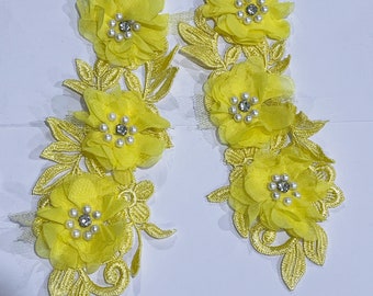 May include: Two yellow floral appliques. Each applique features three chiffon-like flowers with pearl and rhinestone centers, and embroidered leaves. The appliques are ideal for embellishing garments or craft projects.