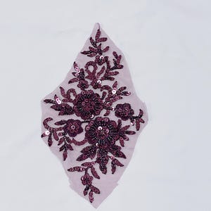 May include: A burgundy floral applique with sequins on a sheer mesh fabric.