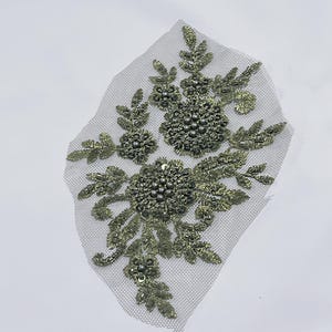 May include: A green floral applique with pearl embellishments on a sheer mesh fabric. The applique is perfect for adding a touch of elegance to clothing, accessories, or home decor projects.