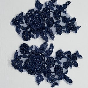 May include: Two navy blue floral appliques with beaded details. The appliques are made of lace and have a delicate, feminine design.