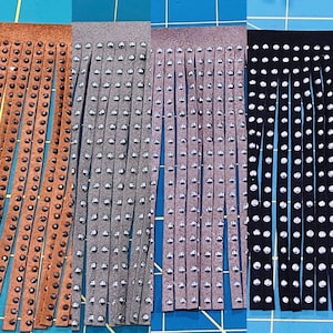 May include: Three strips of leather fringe with silver studs. The fringe is brown, gray, and black.