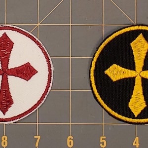 May include: Two embroidered patches with a cross design. One patch has a red cross on a white background, the other has a gold cross on a black background.