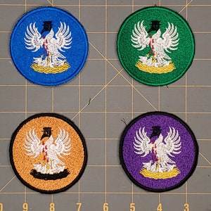 May include: Four embroidered patches with a white bird design. The patches are circular and have a black outline. The bird is depicted with a red heart and is surrounded by smaller white birds. The patches are on a gray background. The patches are blue, green, orange, and purple.