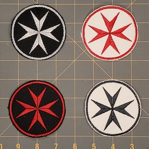 以下が含まれることがあります： マルタ十字のデザインが施された刺繍パッチが4つ。2つのパッチは黒地に白の十字、2つのパッチは白地に赤の十字です。
