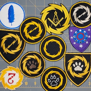 May include: Ten embroidered patches with various designs, including a compass, a paw print, a lightning bolt, and a number 3. The patches are all yellow and black with a white background.