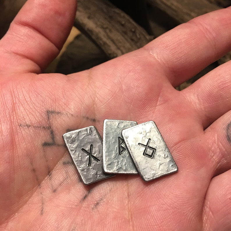 May include: Four silver metal tokens with different symbols etched on them. The tokens are arranged in a pile on a hand.