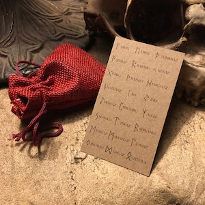 May include: A close-up of a small red burlap bag with a drawstring closure. The bag is sitting on a brown surface next to a card with the names of the runes written in black ink. The runes are: Fehu, Uruz, Thurisaz, Ansuz, Raidho, Kenaz, Gebo, Wunjo, Hagalaz, Nauthiz, Isa, Jera,  Perthro, Algiz, Sowilo, Tiwaz, Berkano,  Mannaz, Laguz, Ingwaz, Dagaz, Othala.