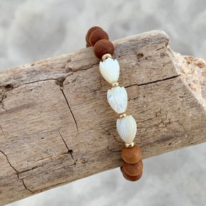 Peut inclure: Un bracelet en perles de bois brun avec trois perles de fleurs en coquillage blanc et des accents dor&eacute;s.