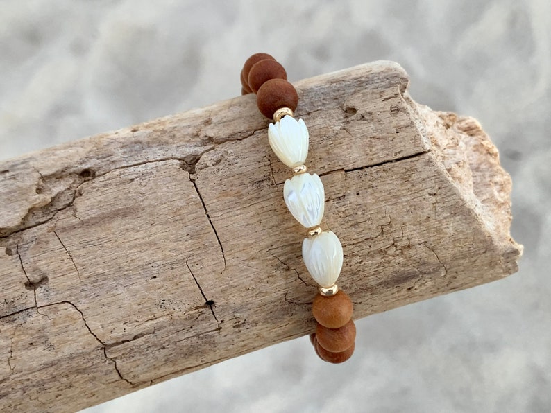 Peut inclure: Un bracelet en perles de bois brun avec trois perles de fleurs en coquillage blanc et des accents dor&eacute;s.