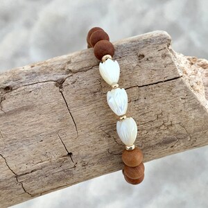 Peut inclure: Un bracelet en bois brun avec trois perles de fleurs en coquillage blanc.