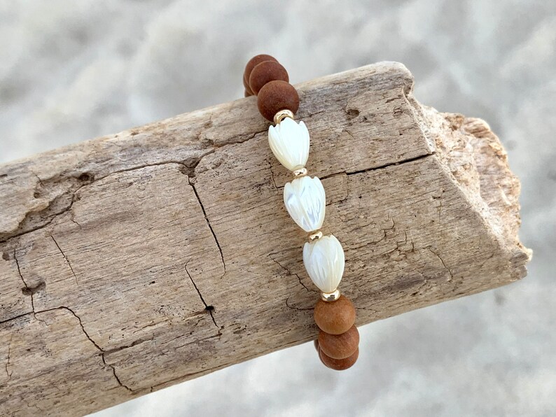 Peut inclure: Un bracelet en bois brun avec trois perles de fleurs en coquillage blanc.