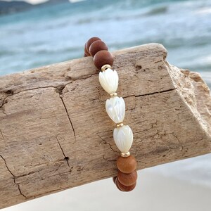Peut inclure: Un bracelet en bois brun avec trois perles de fleurs en coquillage blanc et des accents dor&eacute;s.