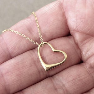 May include: A gold-toned necklace featuring a delicate, open-frame heart pendant suspended from a thin, matching metal chain. The heart design is smooth and minimalist, with a polished finish that reflects light, creating a simple and elegant look.