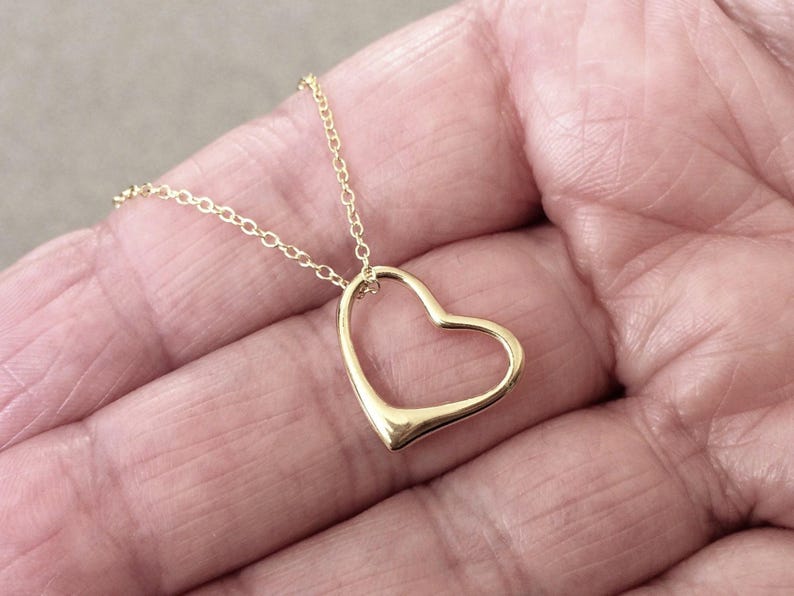 May include: A gold-toned necklace featuring a delicate, open-frame heart pendant suspended from a thin, matching metal chain. The heart design is smooth and minimalist, with a polished finish that reflects light, creating a simple and elegant look.