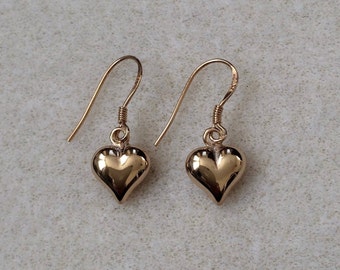 May include: A pair of gold heart-shaped dangle earrings. The earrings have a simple design and are perfect for everyday wear.