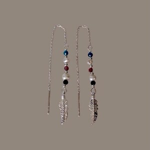 May include: A pair of silver dangle earrings with a feather charm. The earrings feature a chain with blue, red and white beads.
