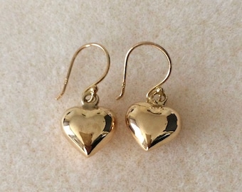 May include: A pair of gold heart-shaped dangle earrings. The earrings are made of a smooth, shiny metal and have a simple, elegant design.