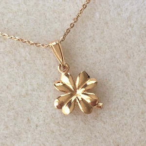 May include: A gold four-leaf clover pendant necklace. The pendant is made of gold and has a shiny finish. The necklace is on a delicate chain.
