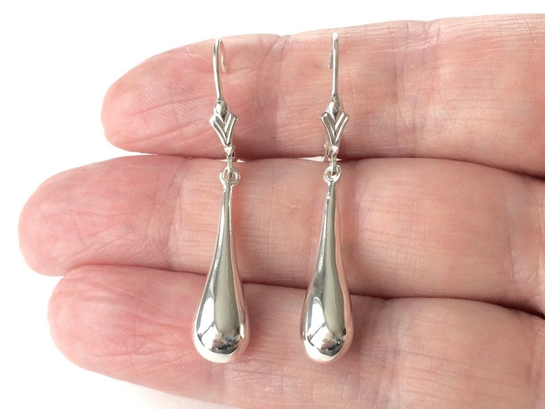May include: A pair of silver teardrop dangle earrings with a simple, elegant design.