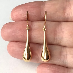 May include: A pair of gold teardrop-shaped dangle earrings. The earrings are made of a smooth, shiny metal.