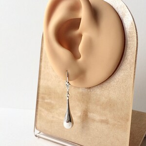 May include: Silver teardrop dangle earrings with a delicate design. The earrings are shown on a display stand.