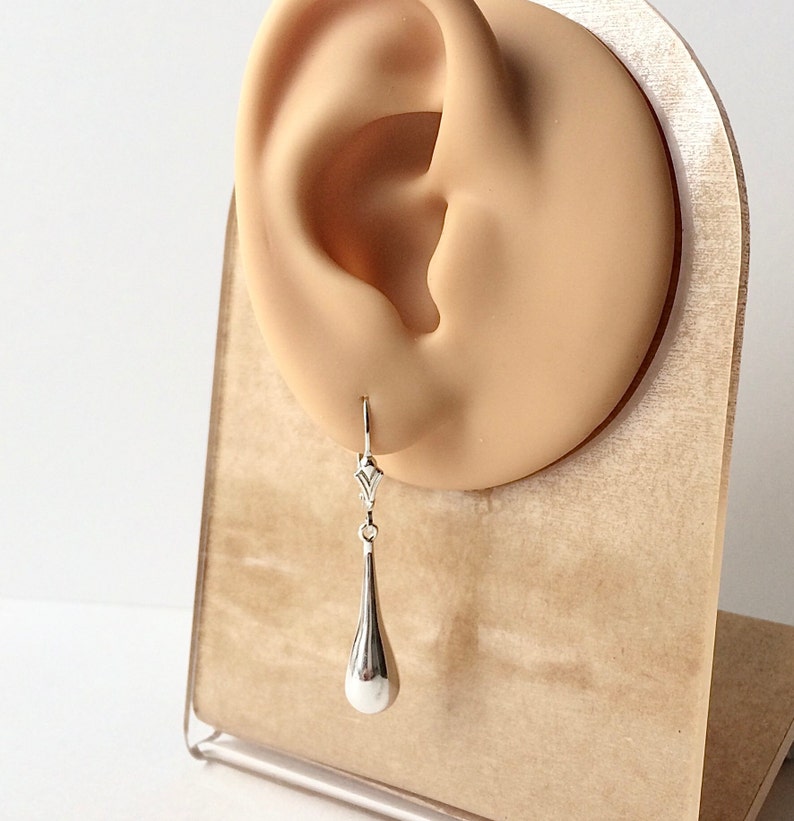 May include: Silver teardrop dangle earrings with a delicate design. The earrings are shown on a display stand.
